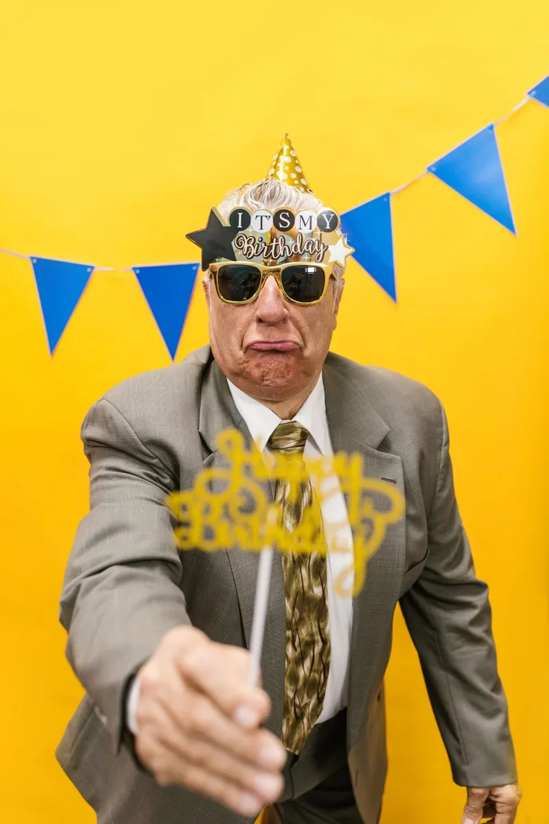 Geburtstagsgast mit Partybrille vor gelbem Hintergrund
