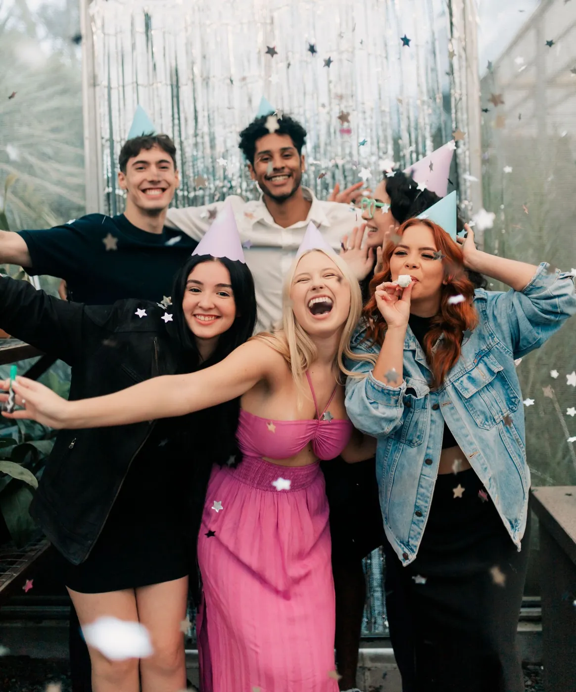 Freunde mit Partyhüten vor einem Silbervorhang